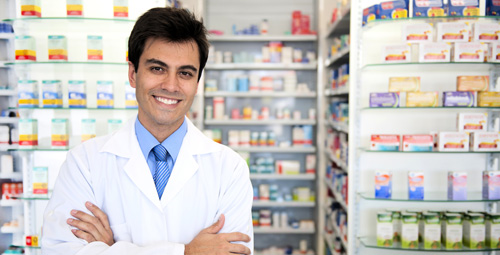 A pharmacist stood with his arms crossed smiling in front of medication shelves
